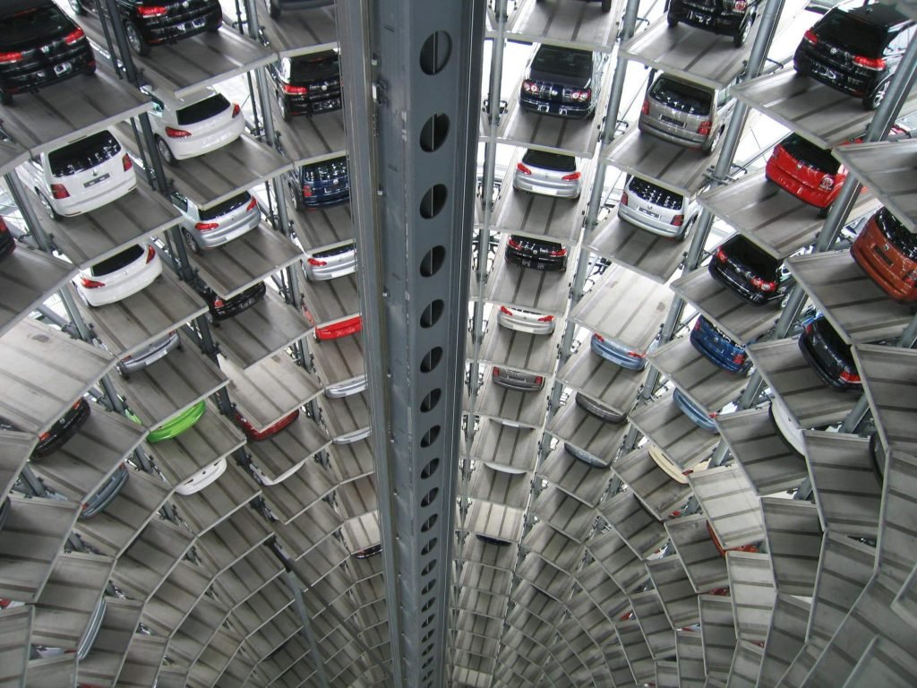 A vertical view inside a futuristic, spiral parking garage with multiple levels, each holding cars in organized rows, creating a sense of depth and complexity.