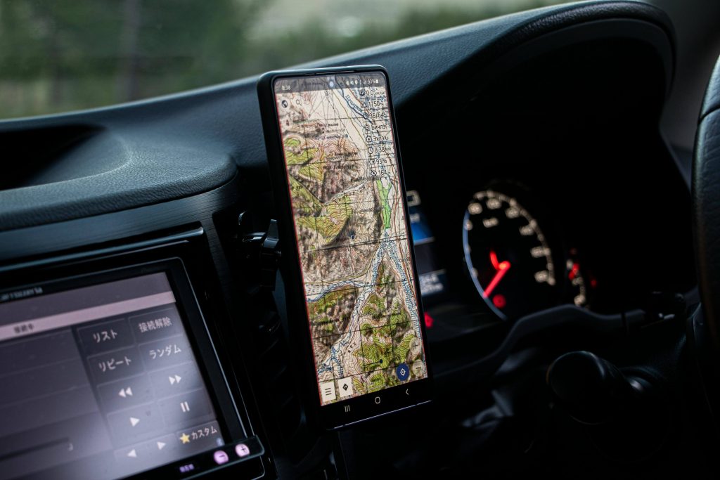 Smartphone with a detailed map displayed is mounted on a car dashboard next to the speedometer, suggesting navigation during a drive.