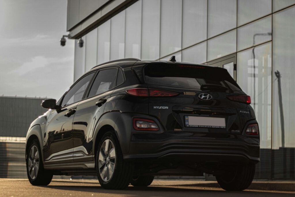 A black SUV parked near a modern glass building, viewed from the rear, with sunlight casting reflections. The atmosphere is sleek and contemporary.
