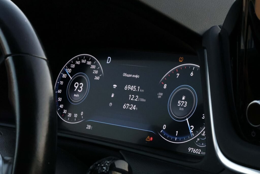 Close-up of a car's digital dashboard displaying speed at 93 km/h, distance traveled, fuel range, and other metrics. The tone is modern and high-tech.