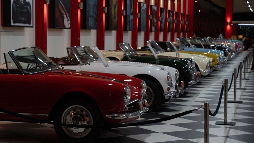 Row of classic convertible cars in various colors, displayed indoors on a black-and-white checkered floor. The setting feels elegant and nostalgic.