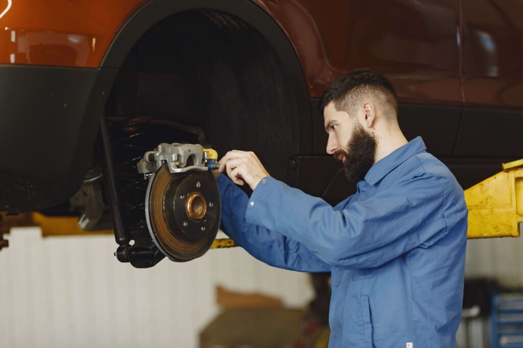 Auto mechanic inspecting and servicing a vehicle's brake disc and caliper while the car is raised on a hydraulic lift in a professional repair workshop.