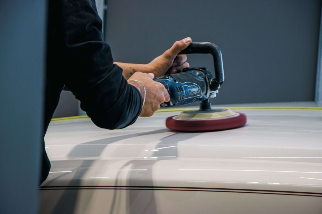Close-up of a technician using a rotary polishing machine to restore the glossy finish of a white car during a professional auto detailing service.