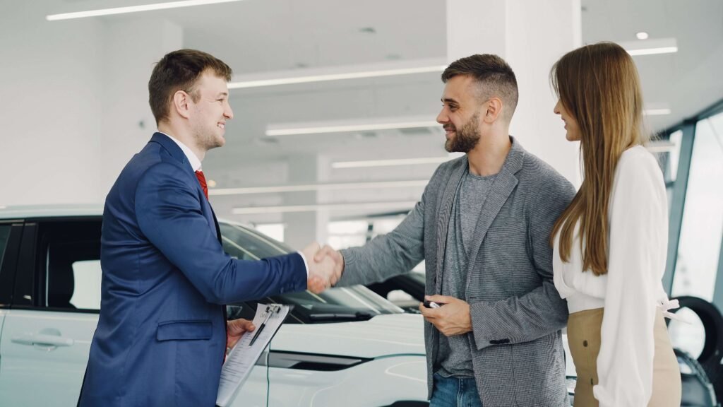 A car buyer shakes hands with a dealership representative in a blue suit while successfully finalizing the process to sell a car in Dubai.