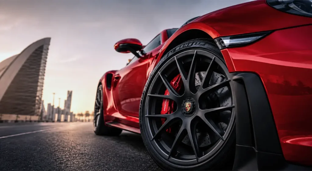Low-angle view of a sleek red sports car with black alloy wheel and red brakes on a city bridge, creating a bold, dramatic mood.