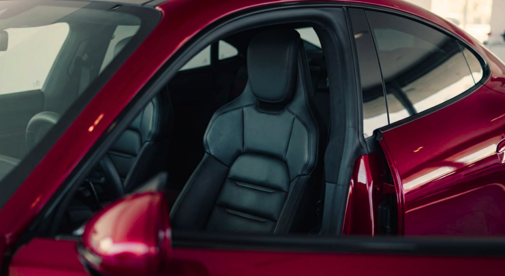 Open driver’s door of a sleek red car reveals a black leather sport seat, modern interior, and glossy bodywork; polished, luxurious tone.